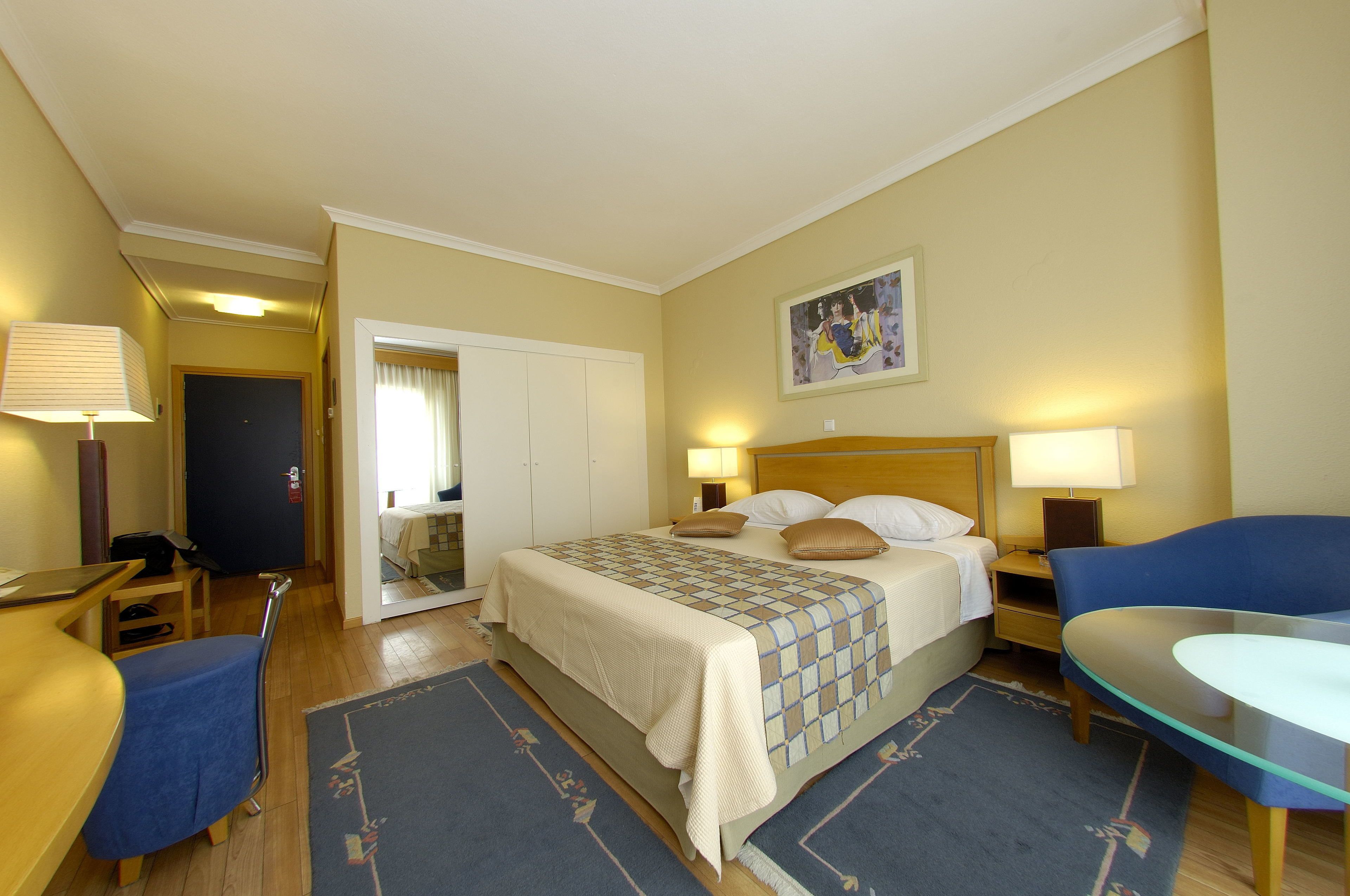 A hotel room with a bed, two bedside tables with lamps, a desk, a chair, and a small table.