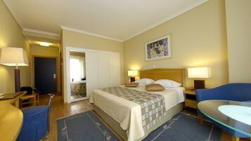 A hotel room with a bed, two bedside tables with lamps, a desk, a chair, and a small table.