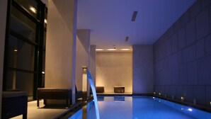 A modern indoor swimming pool with a minimalist design, featuring a clear pool area, a bench, and a wall with a geometric pattern. - Egnatia City Hotel & Spa (Kavala)