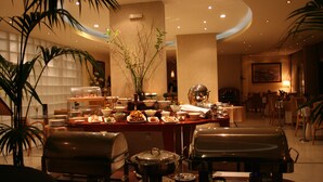 A buffet setup with various dishes, a central vase with greenery, and a seating area with chairs and tables. - Egnatia City Hotel & Spa (Kavala)
