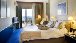 A hotel room with a large bed, a desk with a telephone, a chair, and a view of the sea through the window. - Egnatia City Hotel & Spa (Kavala)