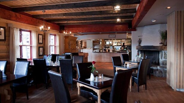 A restaurant with wooden beams, a bar area, and a stone fireplace. - Bykle Hotell  (Bykle)