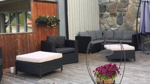 A covered outdoor seating area with a stone wall, wooden deck, and a hanging planter with flowers. - Bykle Hotell  (Bykle)