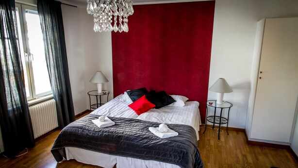 Una habitación de hotel con una cama grande, dos mesitas de noche con lámparas, una pared de acento roja y un candelabro.
