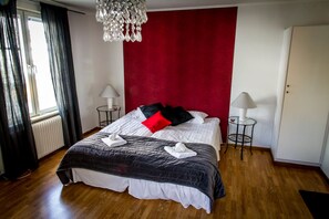 A hotel room with a large bed, two bedside tables with lamps, a red accent wall, and a chandelier. - Park Hotell (Ornskoldsvik)