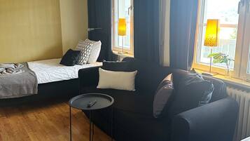 Een hotelkamer met een bed, een slaapbank, een kleine tafel met een afstandsbediening en een raam met gordijnen.