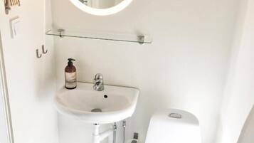 Un baño pequeño y moderno con un lavabo blanco, un espejo redondo, un inodoro y un cubo de basura pequeño.