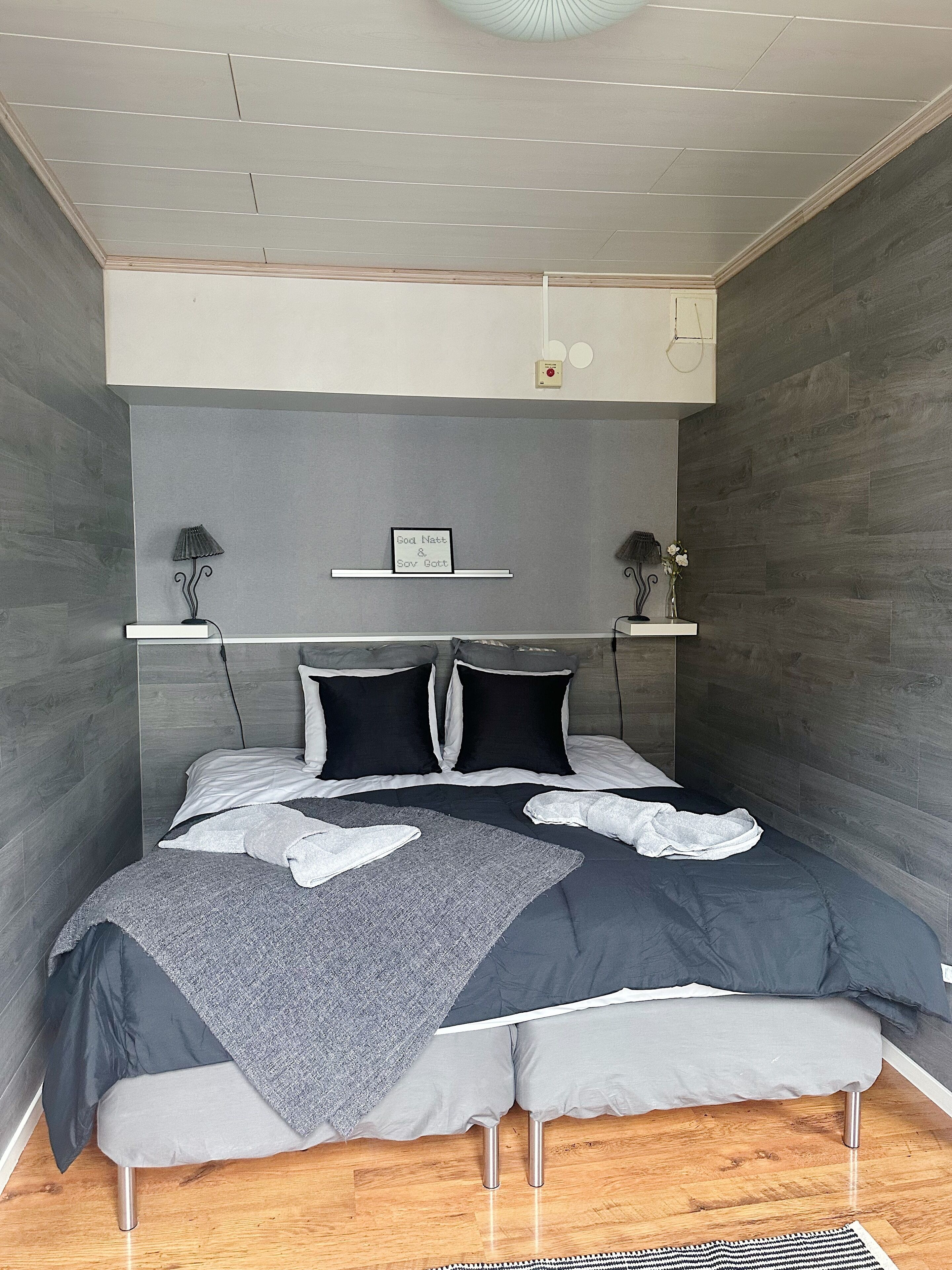 A bedroom with a bed, bedside tables, a wall-mounted shelf, and a ceiling light fixture.