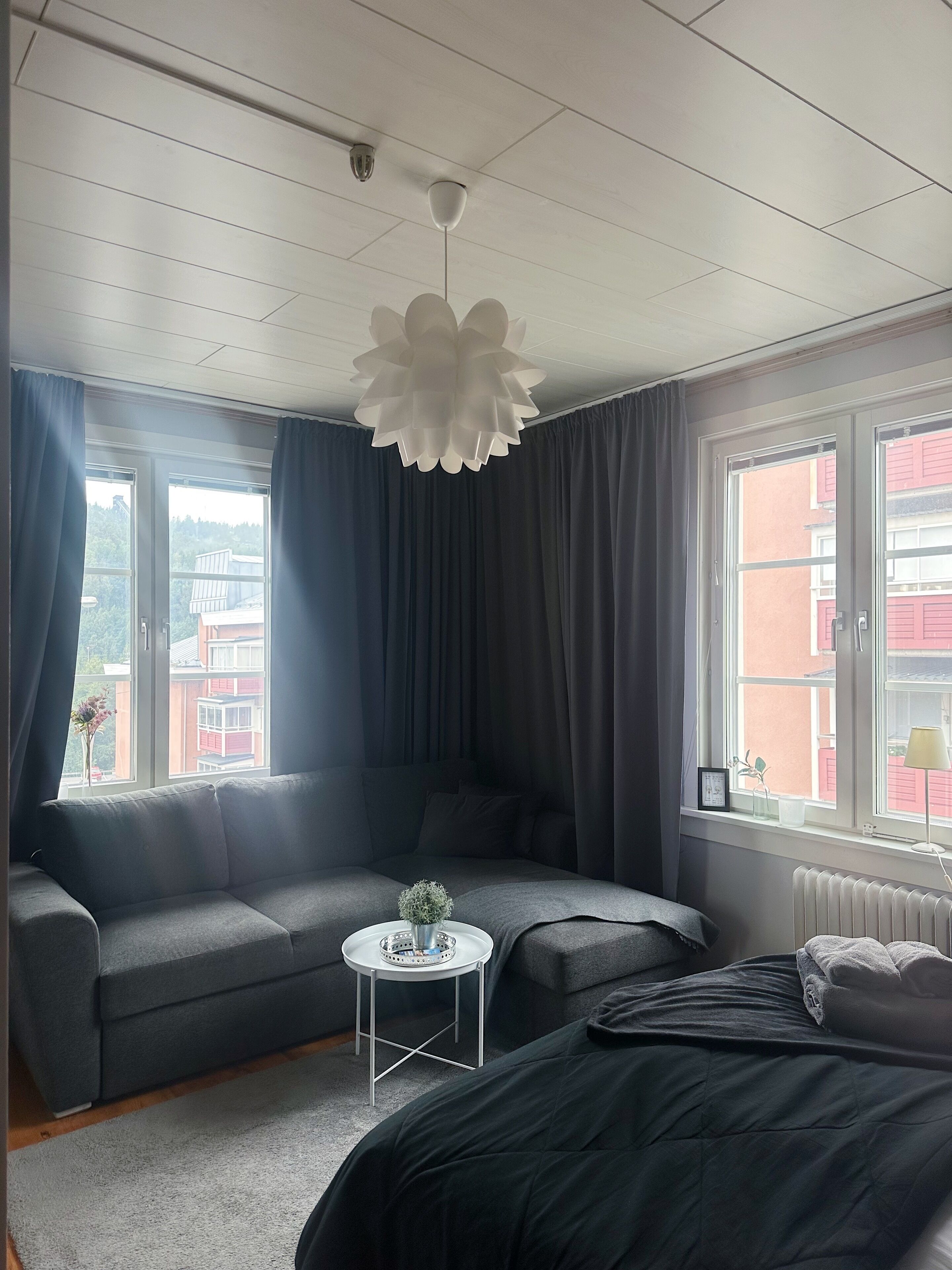A modern bedroom with a grey sofa, a small round table with a plant, and a bed with a grey duvet.