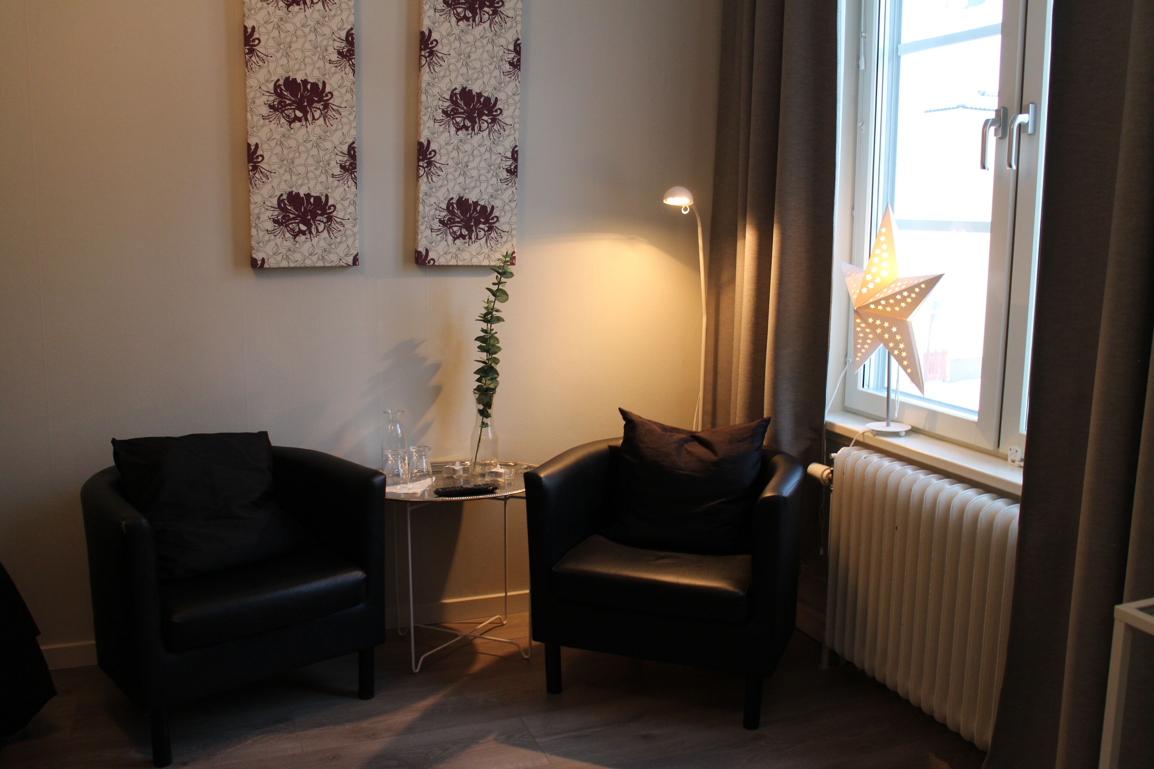 A modern living room with two black leather armchairs, a small table with a vase and glasses, and a star-shaped light decoration.