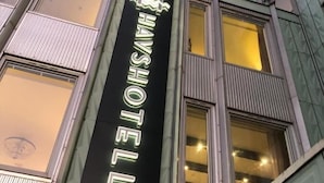 Ein Hotelschild mit einem Kronenlogo und der Schriftzug "HAYSHOTEL" in beleuchteten Buchstaben.