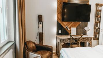 A hotel room with a bed, a desk with a chair, a television mounted on the wall, and a window with curtains.