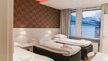 A hotel room with two beds, a window with curtains, a radiator, and a white table.