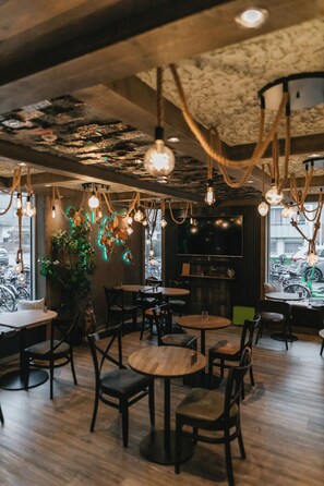 Interior de restaurante con mesas y sillas de madera, lámparas colgantes y un ventanal con bicicletas afuera.