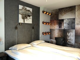 Un dormitorio moderno con una cama grande, dos lámparas de noche, una lámpara de pared y un panel de pared texturizado.