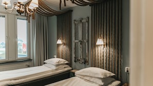 Ein Hotelzimmer mit zwei Einzelbetten, einem Vorhangfenster, einer Chandelierleuchte und einem Wandradiator.
