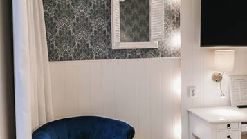 Una habitación con un sillón azul, un escritorio blanco, un espejo y papel tapiz estampado.