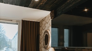 Ein gemütliches Zimmer mit Holzbalkendecke, einem großen Fenster, einem Holztisch, einem Stuhl und einem Bett.