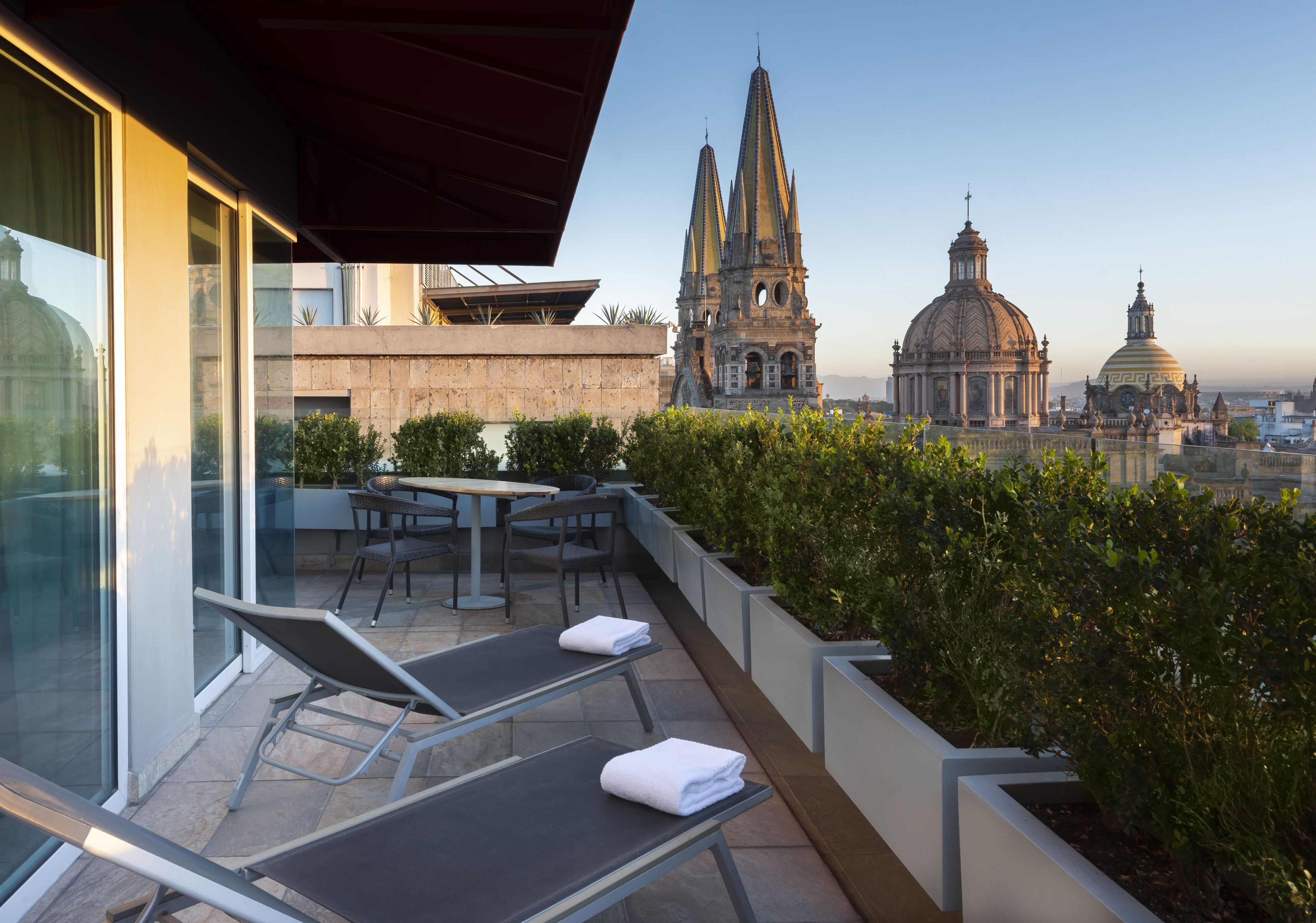 Terraço no telhado com espreguiçadeiras e uma mesa, com vista para edifícios históricos e uma cúpula.