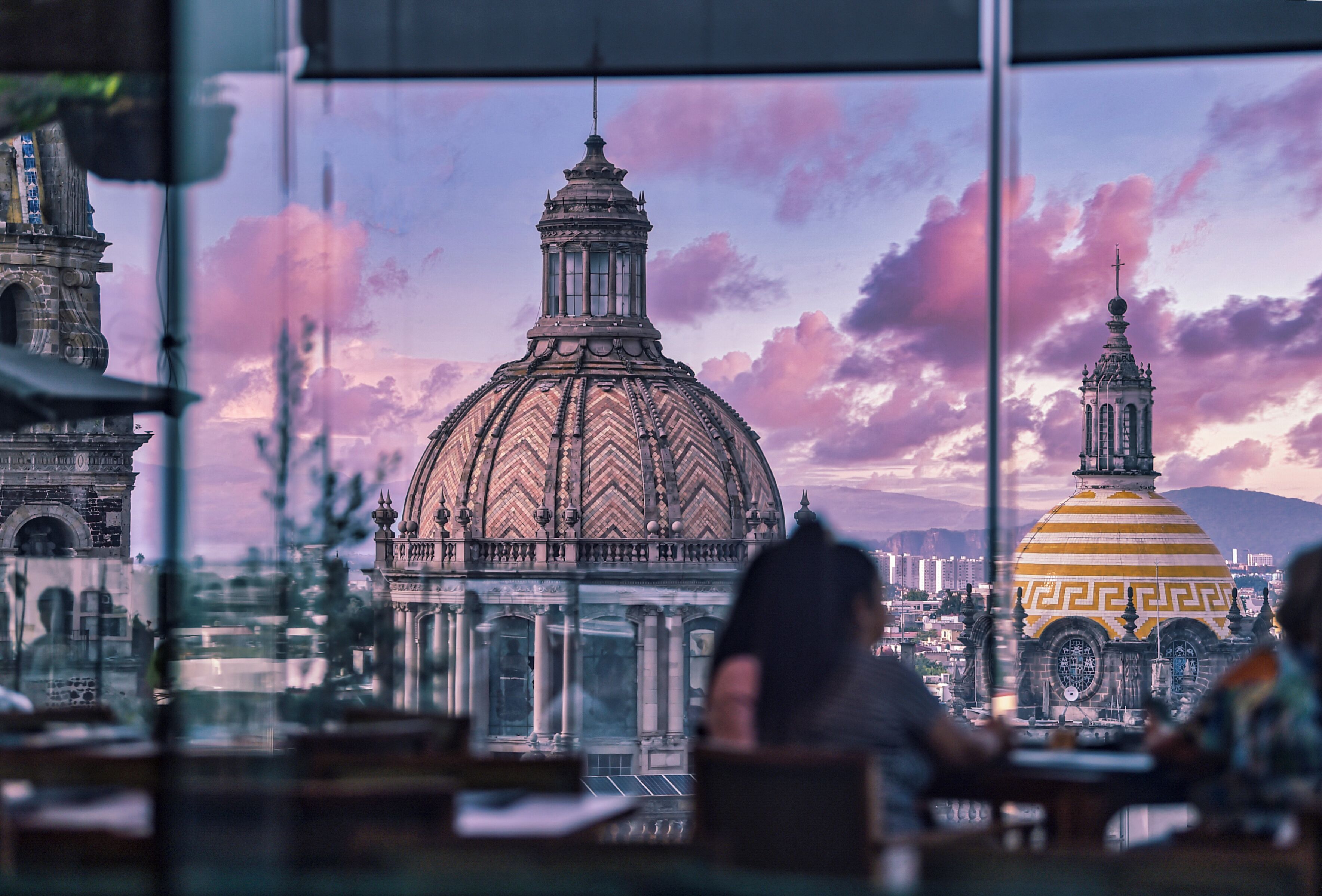A view of a historic building with a large dome and a smaller tower, through a window with a person sitting at a table.