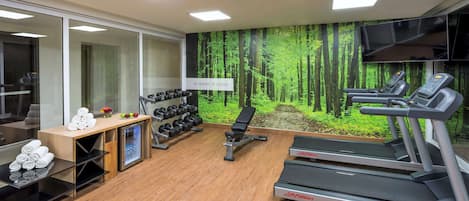 Un gimnasio moderno con cintas de correr, mancuernas y un mural de un bosque en la pared.