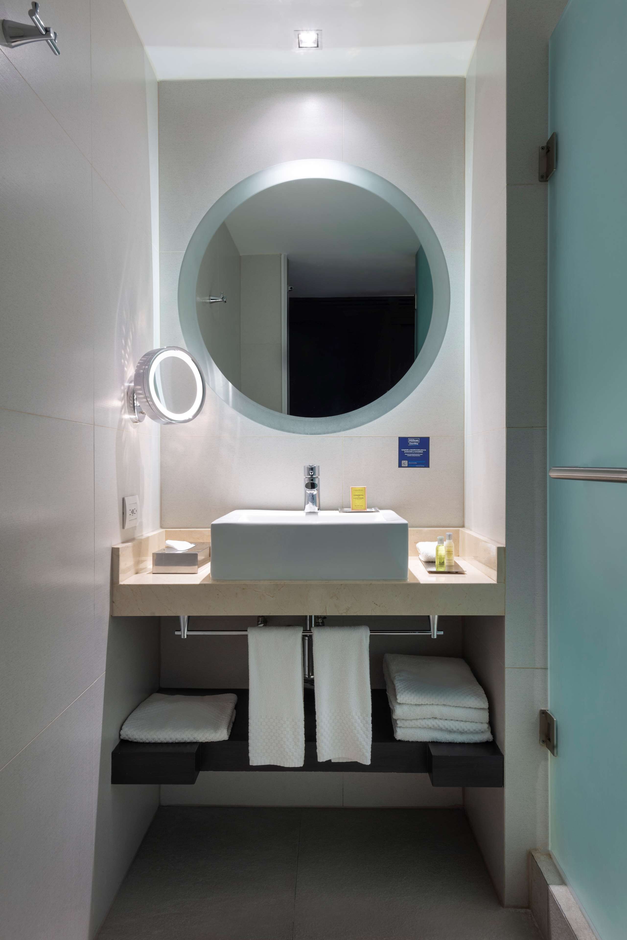 Un baño moderno con un espejo redondo, un lavamanos y un perchero para toallas.