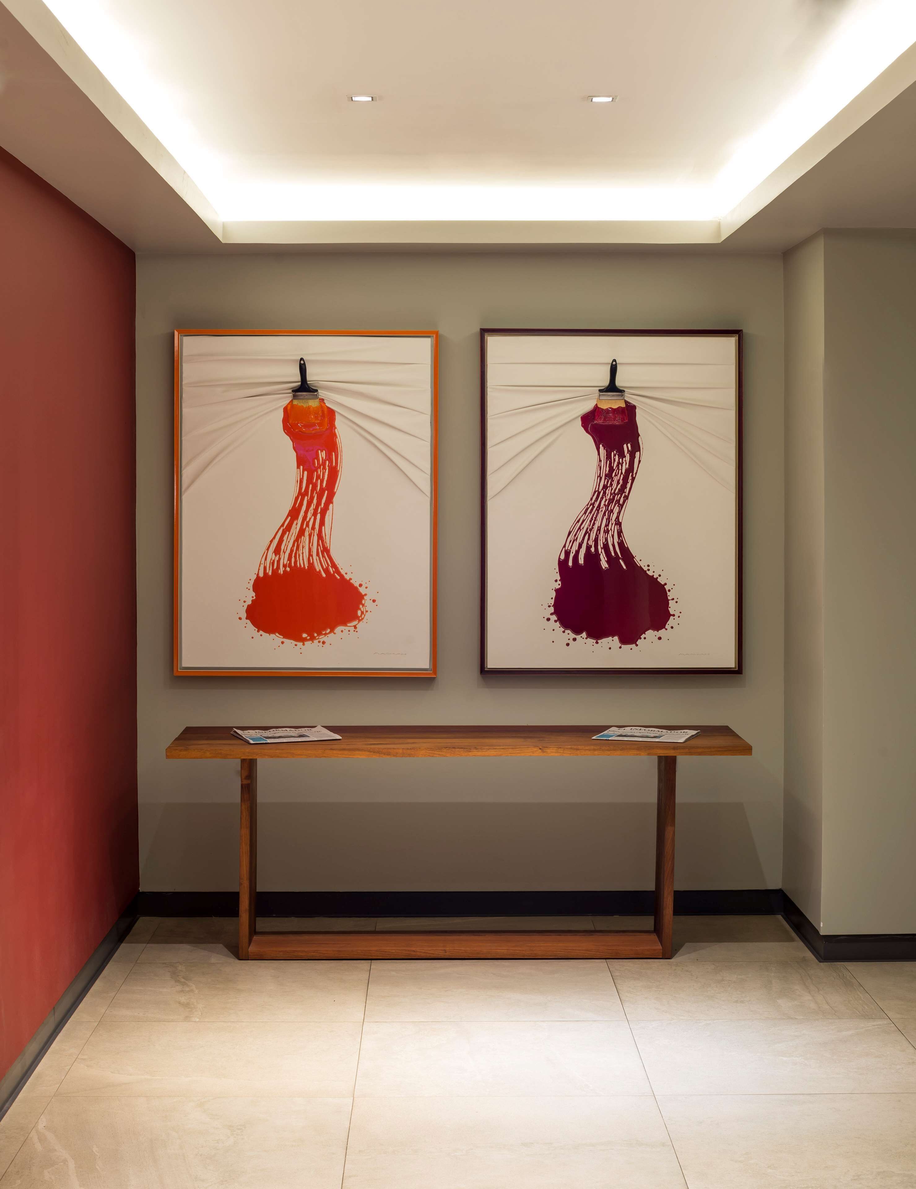 Two framed artworks of dresses on a wall, a wooden bench in the center, and a ceiling light.