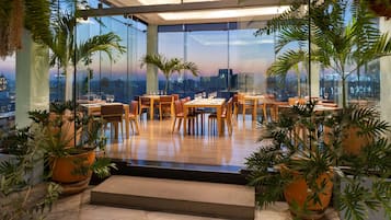 A restaurant with a city view, large windows, and potted plants.