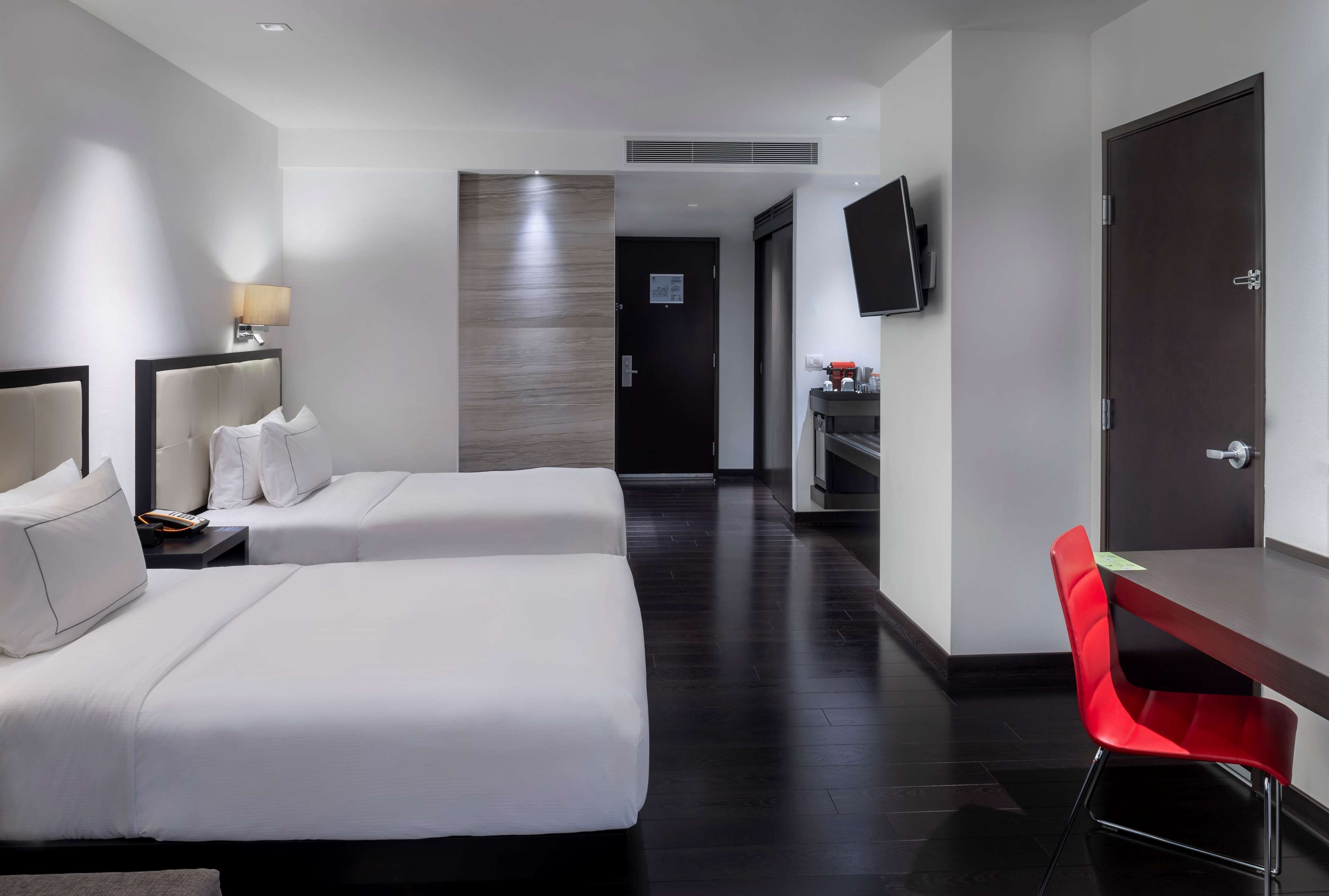 A hotel room with two beds, a desk, a TV, and a red chair.
