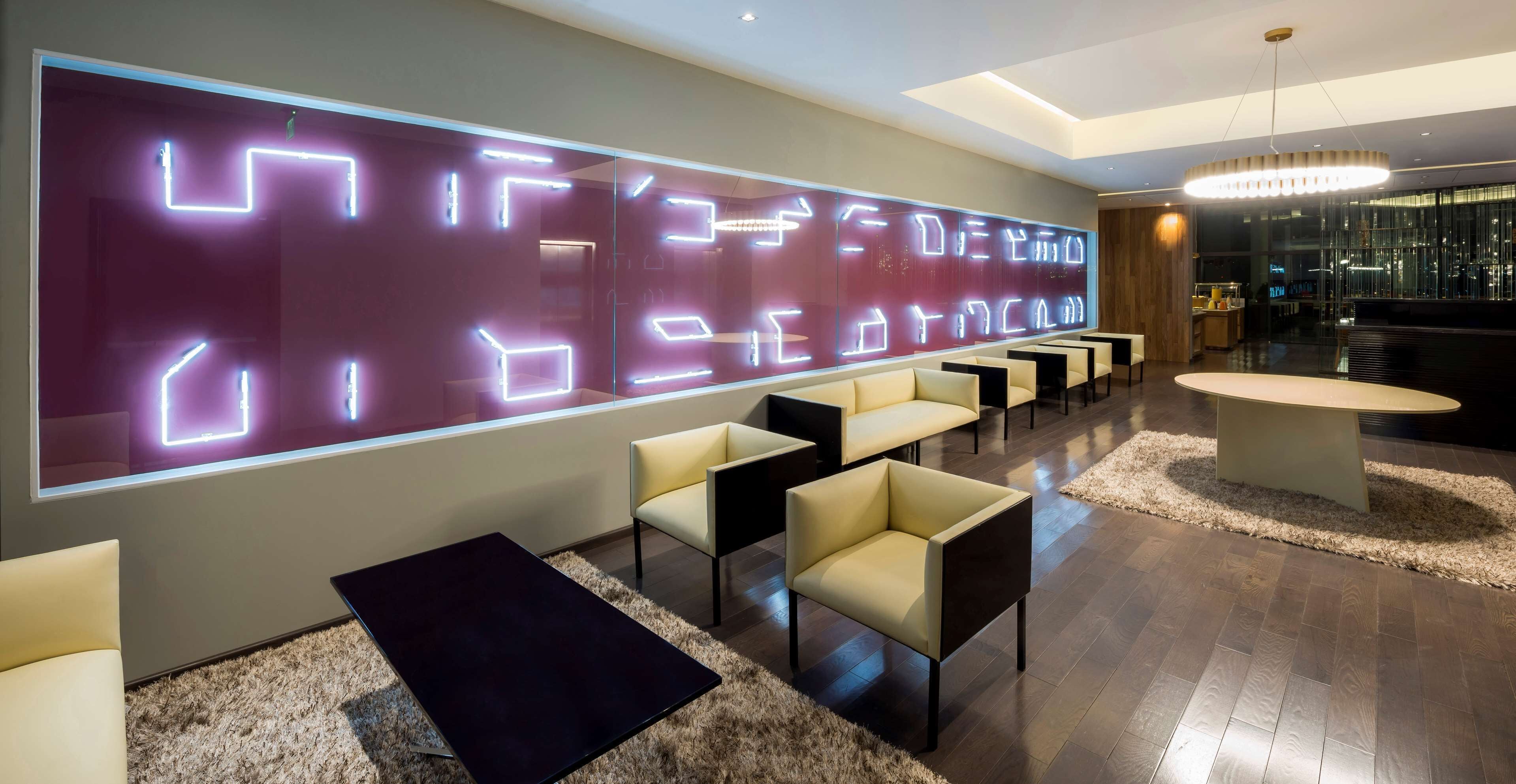 Un vestíbulo moderno con una pared grande iluminada, una zona de estar y una recepción.