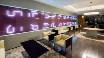 Un vestíbulo moderno con una pared grande iluminada, una zona de estar y una recepción.