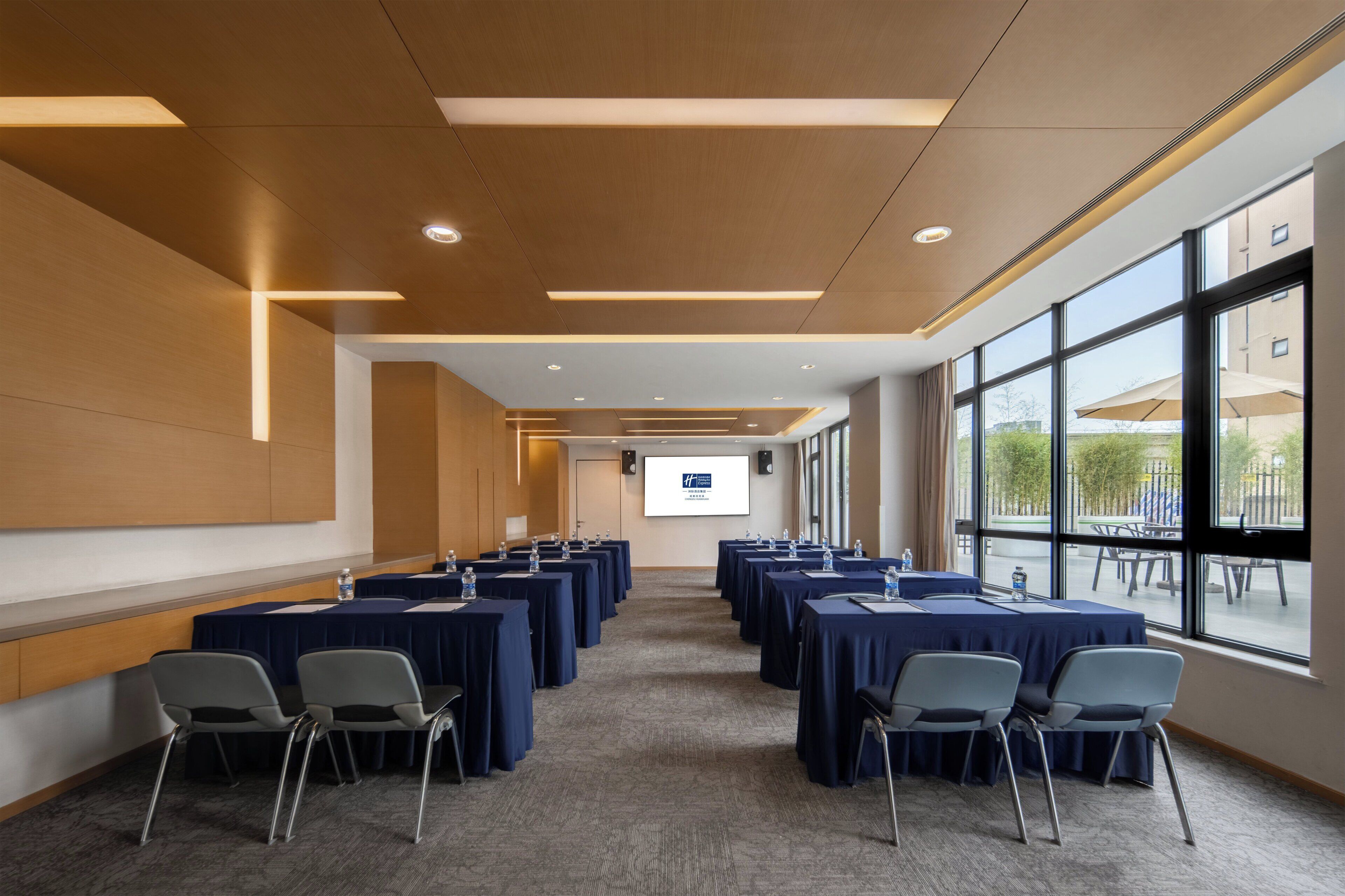 A conference room with tables and chairs, large windows, and a projector screen.
