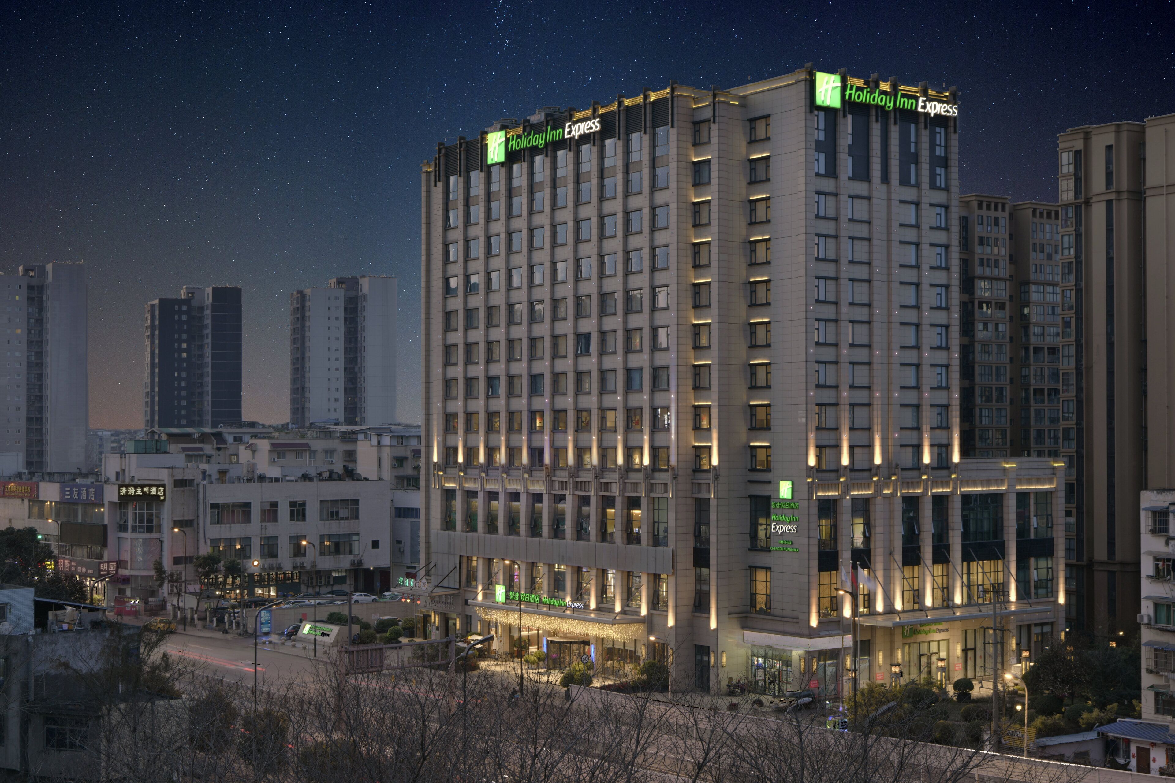 A multi-story hotel with a prominent Holiday Inn Express sign, surrounded by other buildings and a clear night sky.