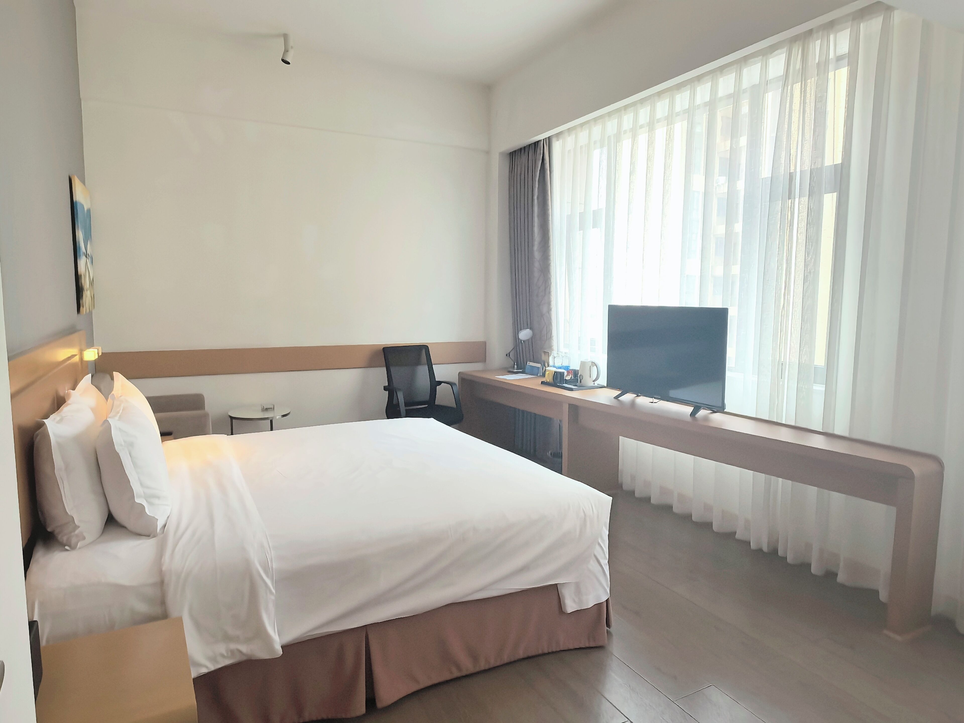 A hotel room with a large bed, a desk with a computer, a chair, and a TV.