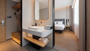 Une chambre d’hôtel moderne avec un grand lavabo, un miroir, une table de chevet, un lit et un petit banc en bois.