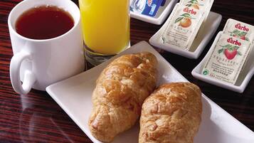 A breakfast setting with a cup of coffee, a glass of orange juice, two croissants, and packets of orange juice and milk.