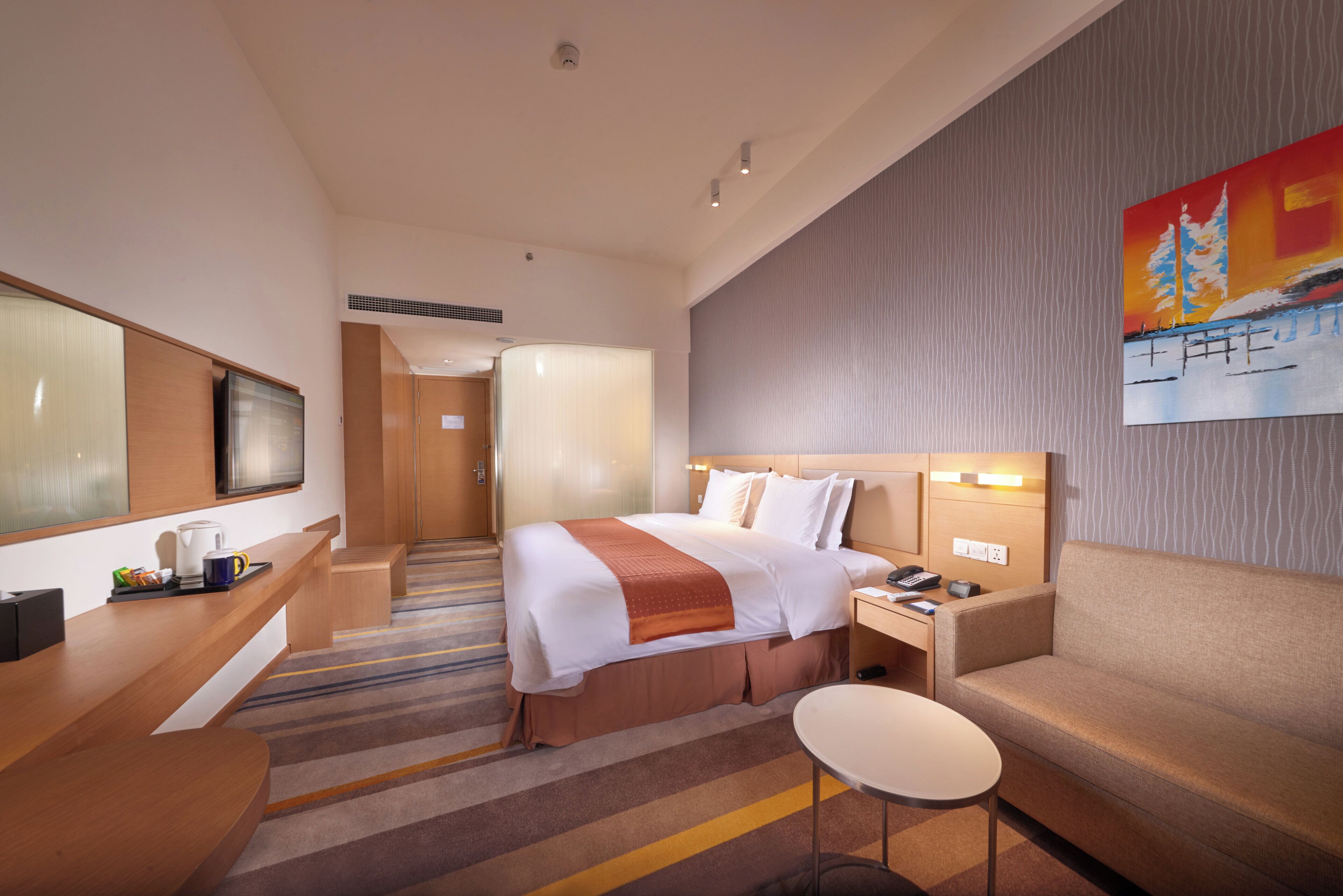 A hotel room with a bed, bedside table, chair, TV, and a painting on the wall.