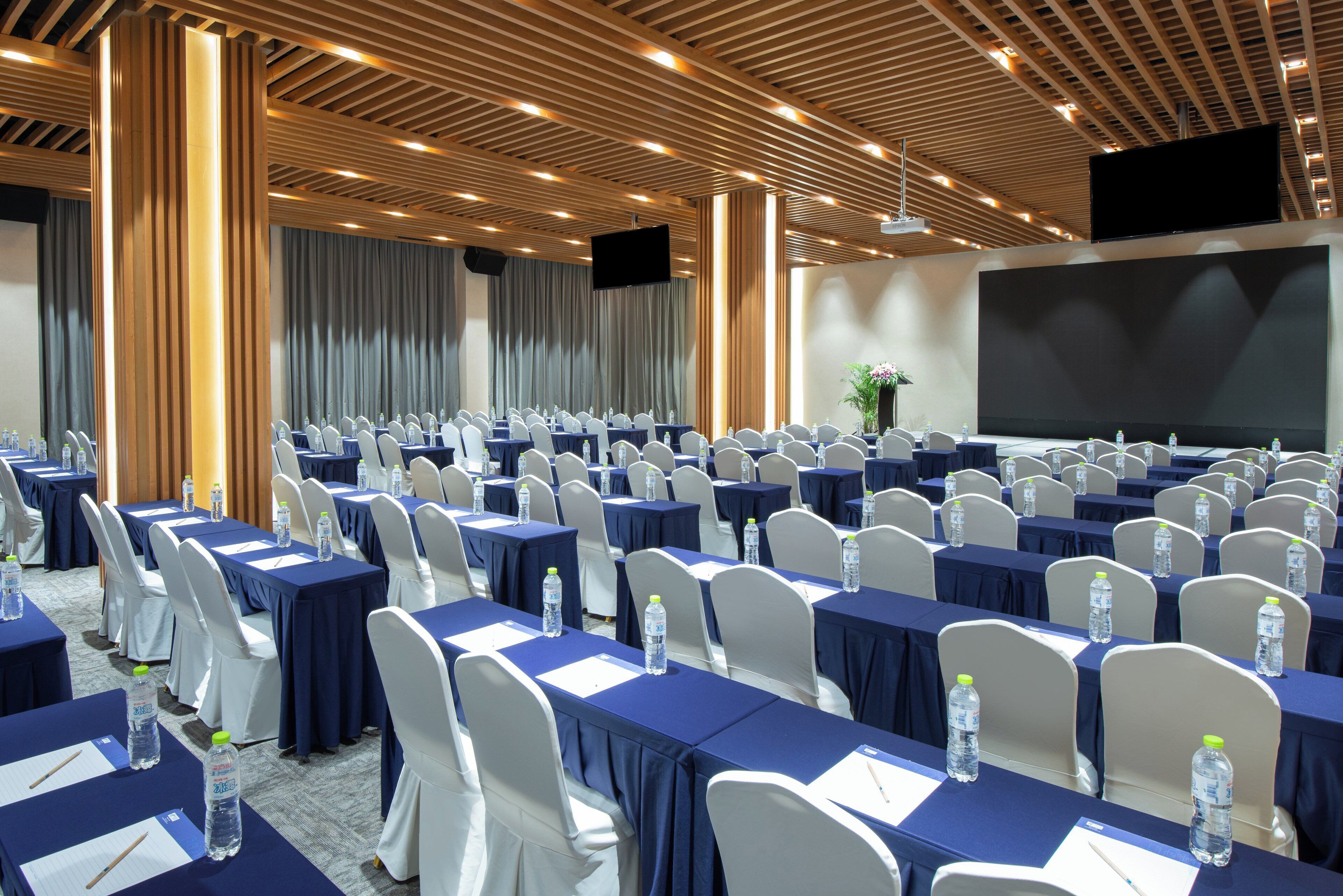 A conference room with rows of tables, chairs, and a large screen for presentations.