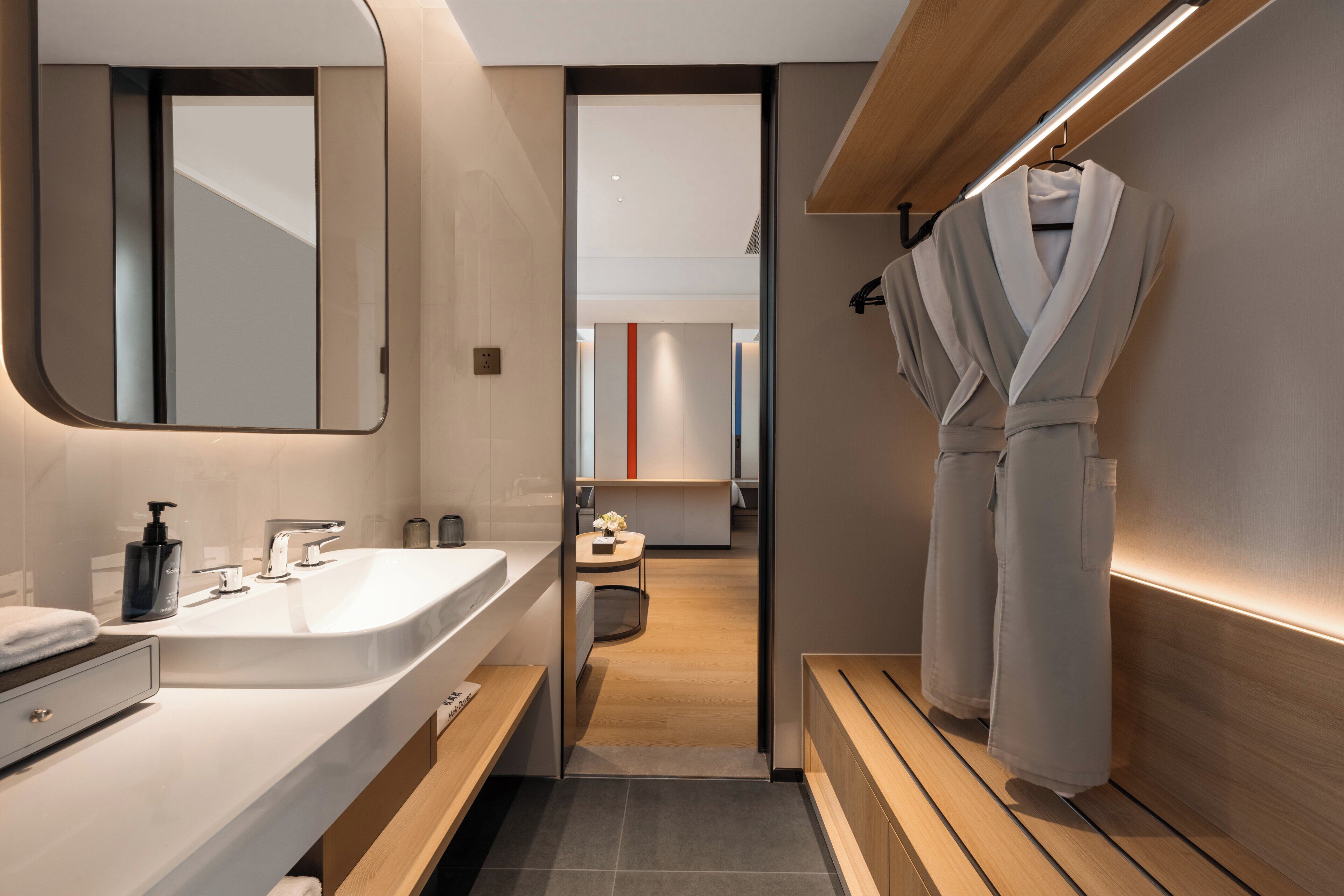 A modern bathroom with a large mirror, a sink, and a robe hanging on the wall.