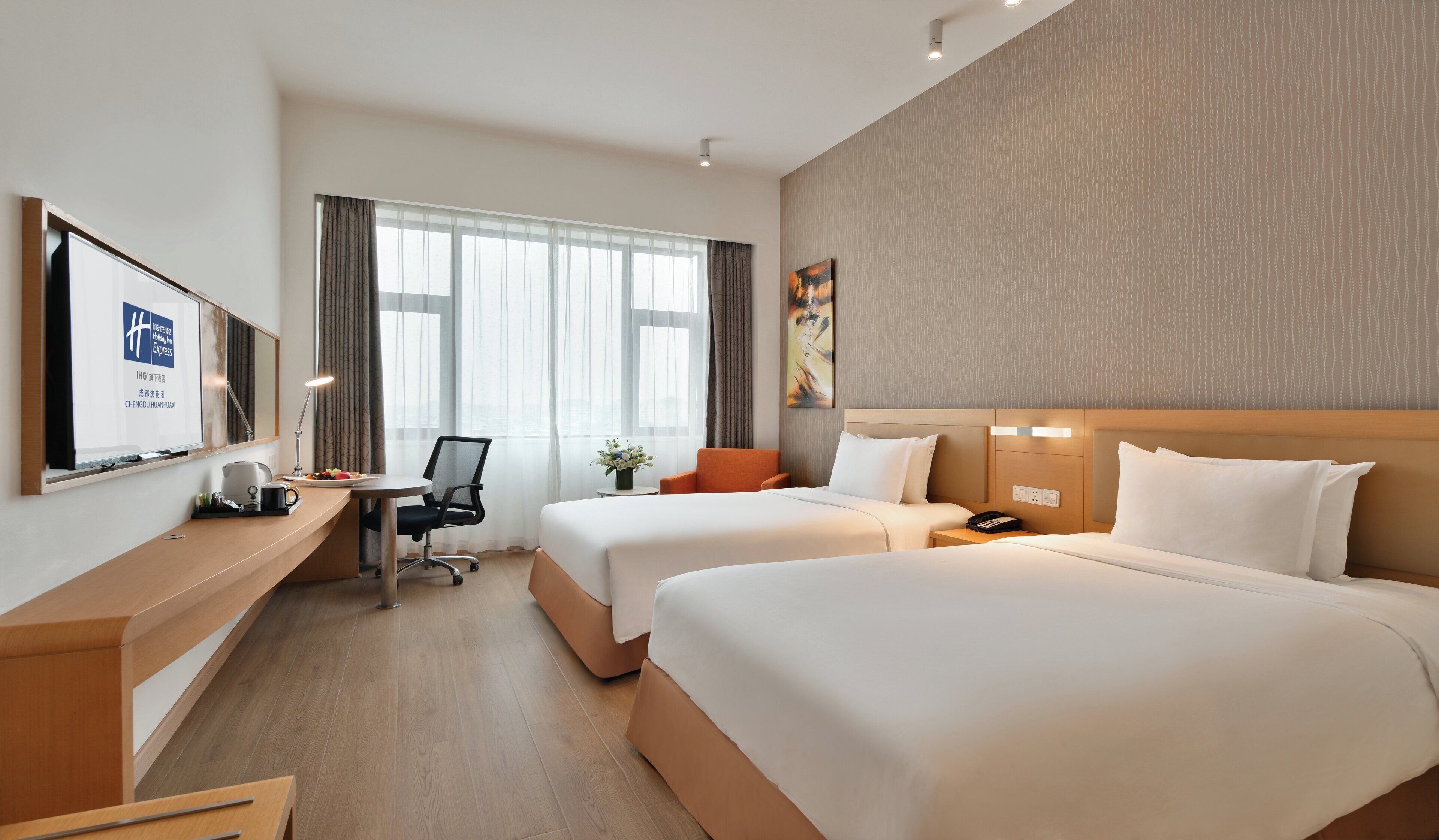 Habitación de hotel con dos camas, un escritorio, una silla, un televisor y una ventana con cortinas.