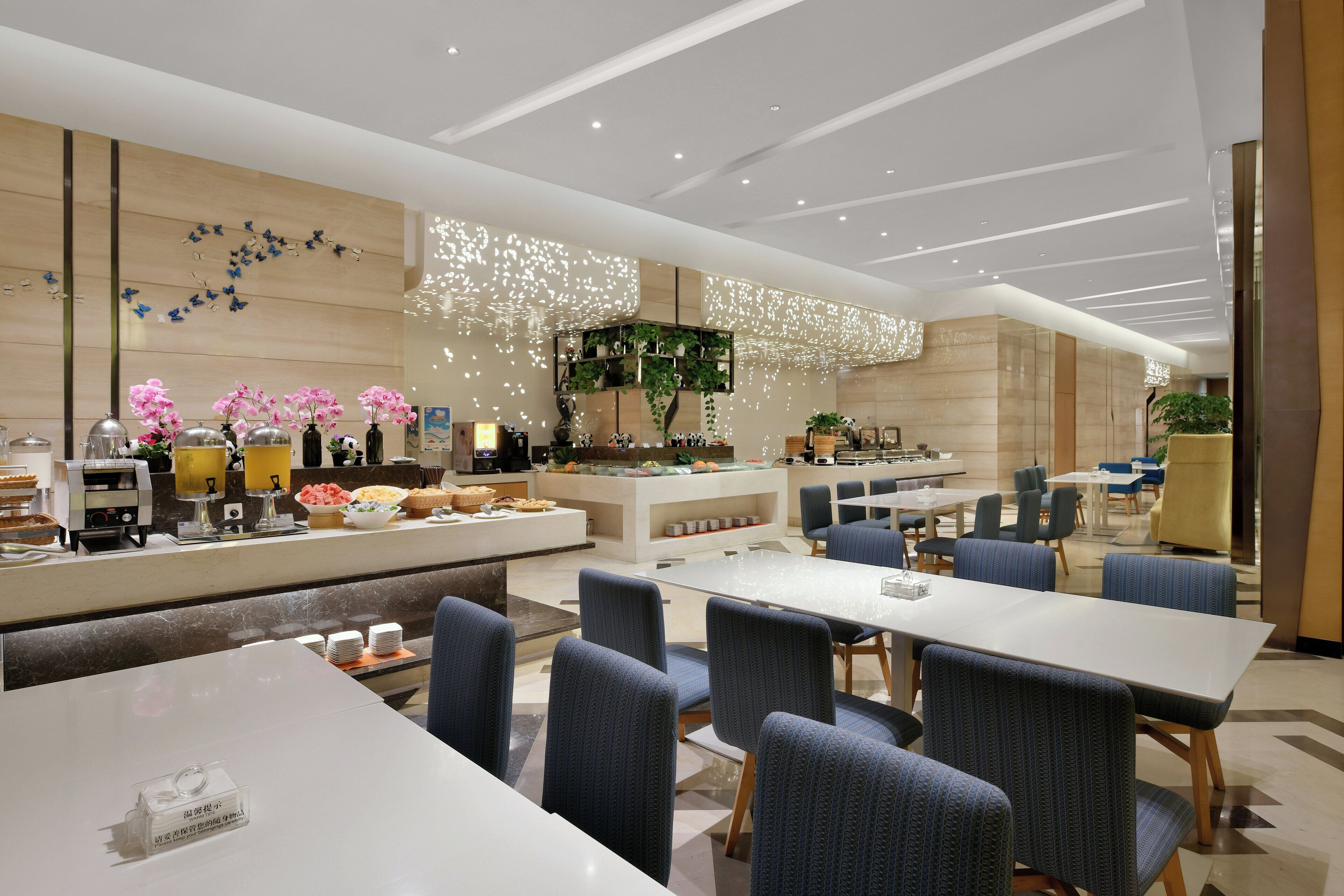 A modern hotel lobby with a central reception desk, seating area, and a decorative wall with plants and butterflies.