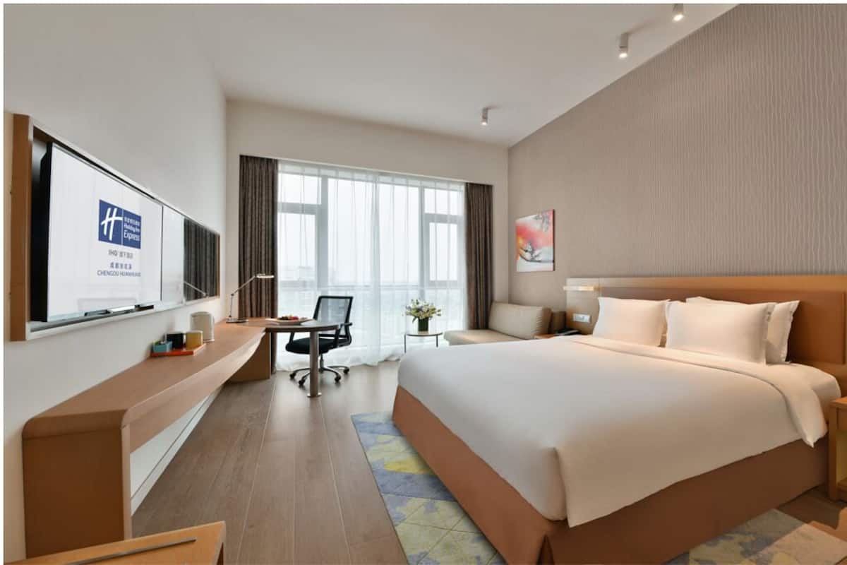 Una habitación de hotel moderna con una cama grande, un escritorio con una silla, televisión y una ventana con cortinas.
