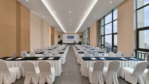 Une salle de conférence avec des rangées de tables et de chaises, un grand écran à l’avant et une vue sur la ville grâce à de grandes fenêtres.