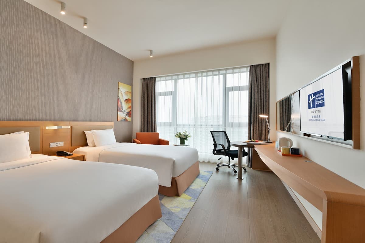 Habitación de hotel con dos camas, un escritorio y un televisor.