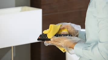 A person wearing gloves and a face shield cleaning a remote control with a yellow cloth.