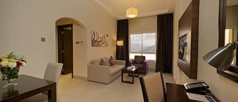 Habitación de hotel con comedor, sofá, una silla, escritorio con lámpara y ventana con vista a montañas.
