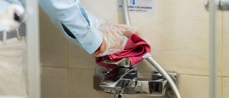 A hand wearing a glove cleaning a shower control panel.