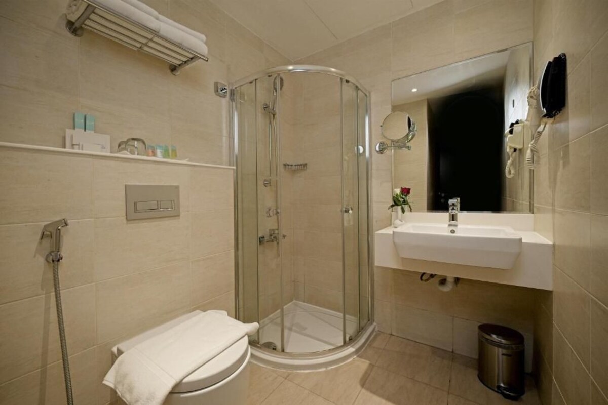 A bathroom with a glass-enclosed shower, a white sink, a mirror, and a towel rack.