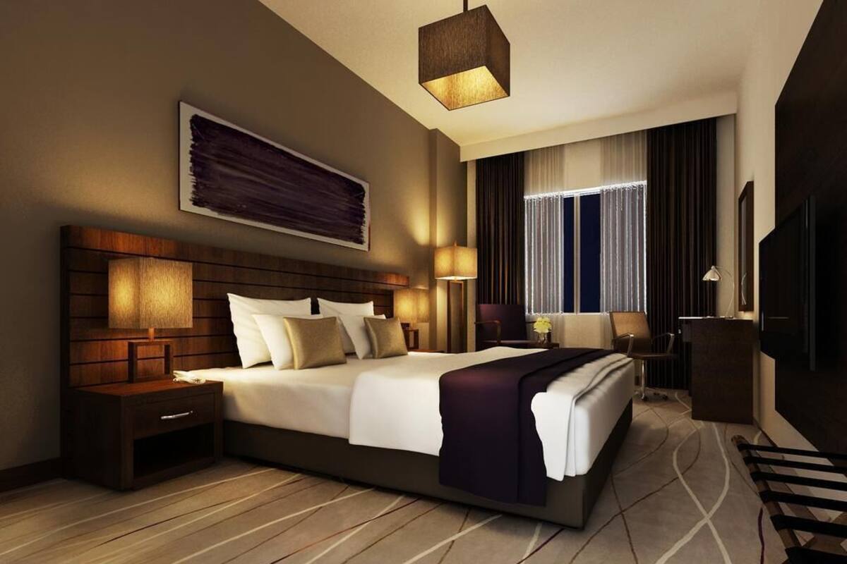 Une chambre d’hôtel moderne avec un grand lit, une tête de lit en bois, des tables de chevet et un téléviseur.