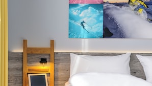 Une chambre à coucher avec une tête de lit en bois, une table de chevet sur laquelle est posée une tablette, et un grand tableau représentant un skieur, accroché au mur.